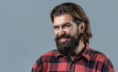 Smiling brutal bearded man holding shampoo bottle on gray background, haircare. Man holds bottle of...