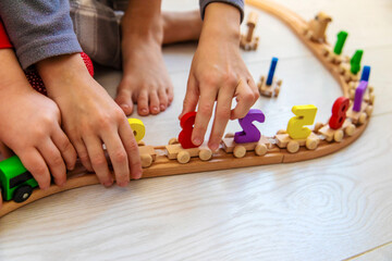 Obraz premium Child playing with a wooden toy train with colorful letters on a light floor.