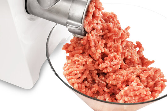 A close-up of fresh, ground meat being extruded from a metal meat grinder and collecting in a clear glass bowl.
