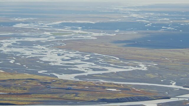 An aerial shot captures the stunning, intricate patterns of a braided glacial river as it flows across a vast, flat outwash plain, known as a sandur, in Iceland