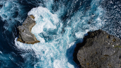Abstract, top down shot of dark sea stacks, near Angel's Billabong, surrounded by dynamic, swirling turquoise water and white foam. © Jens