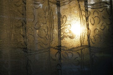 Altertümliche Gardine mit Muster vor goldweißer Sonne bei Sonnenaufgang am Morgen im Herbst