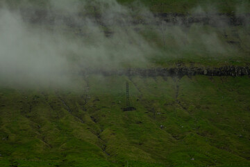 Electric pole standing alone on a fog-covered green mountain in the Faroe Islands — a blend of nature and solitude for travelers exploring remote paths.