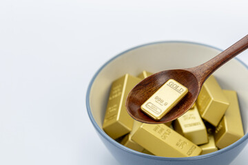 Scooping gold bars with a spoon into a blue and white ceramic bowl on clean white background symbolizing wealth, luxury, and prosperity