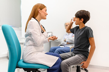 Female doctor explaining to young boy how to use asthma pump during routine checkup at pediatric clinic