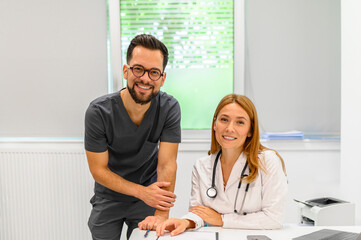 Portrait of smiling male and female doctor colleagues collaborating at desk in hospital during...