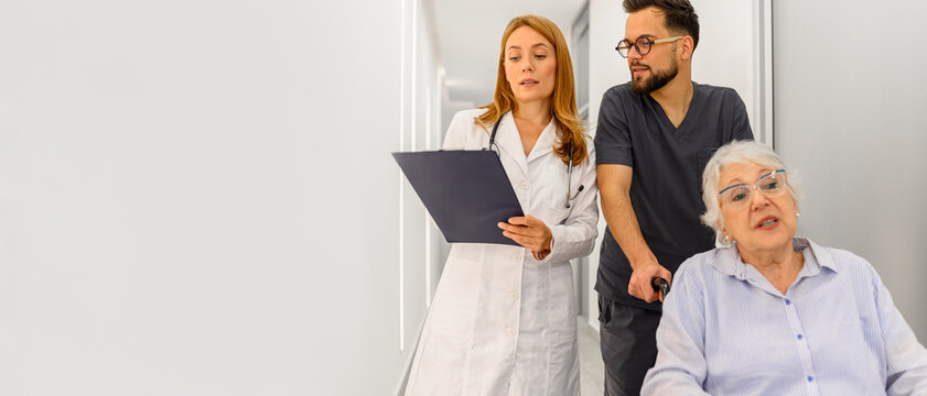 Doctors talking about diagnosis and care strategy while moving with senior woman on wheelchair in hospital corridor