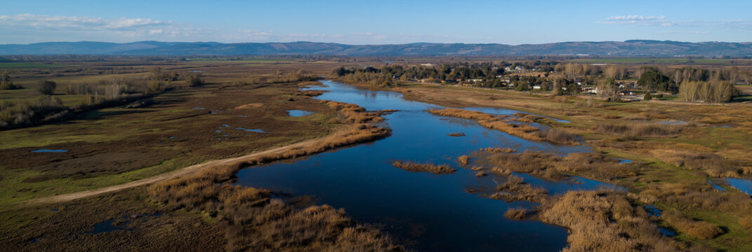 A breathtaking aerial view showcasing a serene river winding through open fields, surrounded by distant hills, exhibiting a tranquil natural landscape under a clear blue sky.