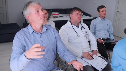 Group of physicians and healthcare workers in shirts and white coats taking part in seminar and listening to colleague during clinical training.