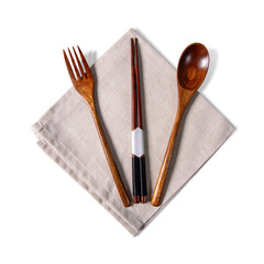 Top view of wooden fork, spoon, and traditional Asian chopsticks placed symmetrically on a beige linen napkin, isolated on a clean white background