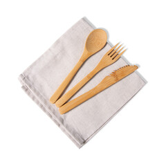 Sustainable and reusable bamboo fork, spoon, and serrated knife set arranged on a neutral beige linen napkin, isolated on a clean white background.