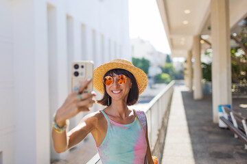Stylish tourist taking photos of city center landmarks with her smartphone. Portrait of happy female traveler with mobile phone taking photos and exploring city landmarks.