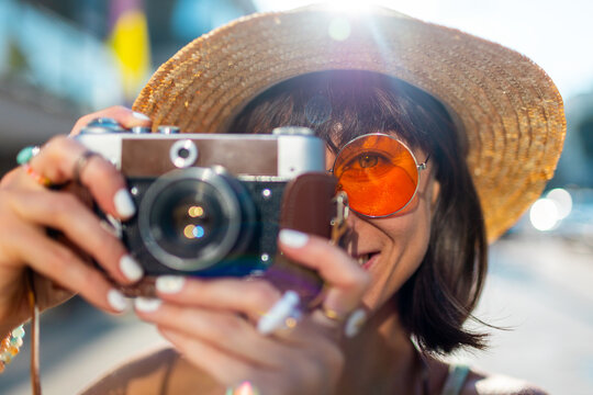 Summer portrait of smiling young woman having fun in city with camera, photographer taking pictures wearing glasses and hat.
