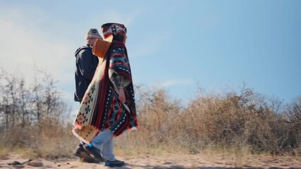 A man and a young woman in an ethnic patterned blanket walk together outdoors, talking and enjoying nature. Relaxed lifestyle, authentic travel, and simple moments of connection in the wild.