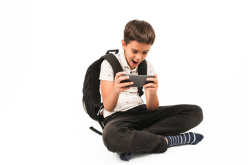 Young boy with backpack sitting cross-legged, holding smartphone and looking excited, isolated on white background. Suitable for illustrating technology use, childhood gaming, or digital learning