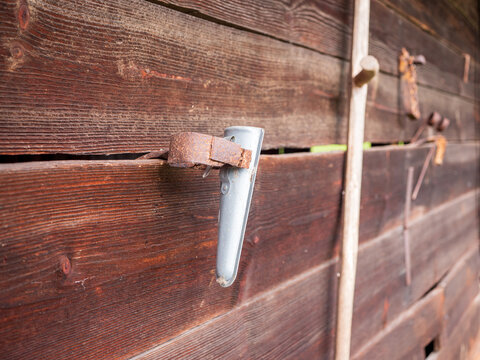 Detail of a rusty metal sheath for a whetstone, hanging on the wooden wall of an old shed used for sharpening a scythe.