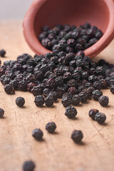 side view of black peppercorns spilling from terracotta pot onto rustic wooden surface, soft focus earthy still-life and culinary spice concept in vertical orientation