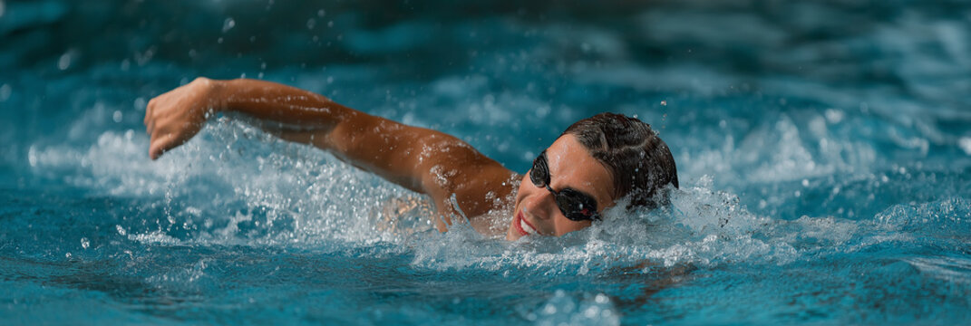 A determined female swimmer with goggles strokes powerfully through the water, embodying strength and athleticism in a competitive swimming environment at a swimming pool.