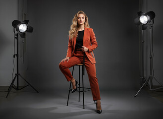 Stylish young woman posing on a stool in an orange suit with studio lights  