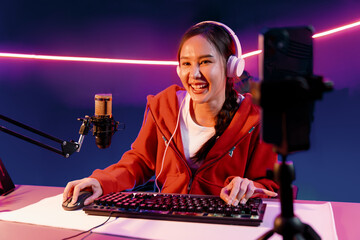 Host channel of smiling beautiful Asian girl streamer playing online game wearing headphone talking...