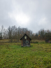 Rustic wooden cabin standing alone in a grassy field under gray sky  