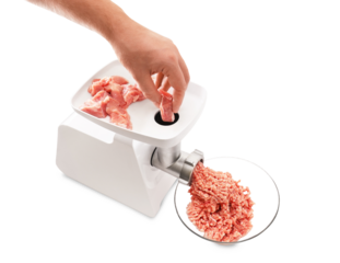 A person's hand pushes a raw piece of pork into a white electric meat grinder, with ground meat collecting in a glass bowl.PNG