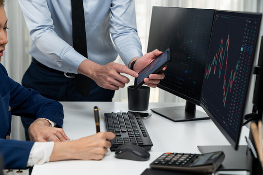 Cropped hand of businessman showing dynamic stock market data on phone to woman writing to memo for analyzing profit value currency rate online website program application at home office. Infobahn.