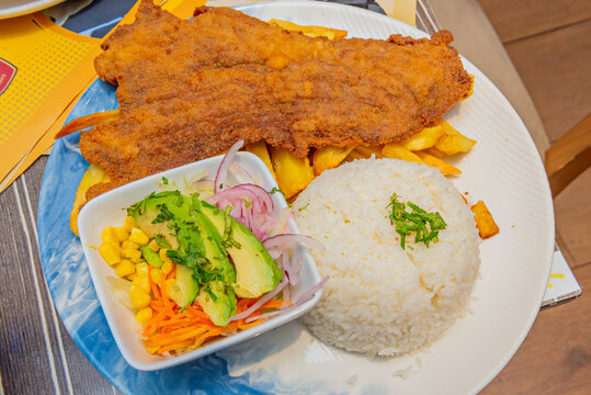 Golden llapingachos are presented on a wooden platter with their characteristic cheese filling, covered in peanut sauce, and accompanied by chorizo ​​and a fried egg