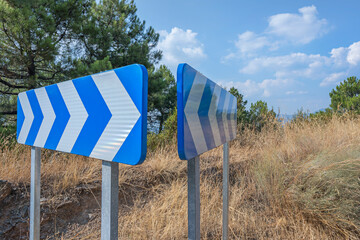 Blue and white directional signs alongside a mountain road surrounded by vegetation