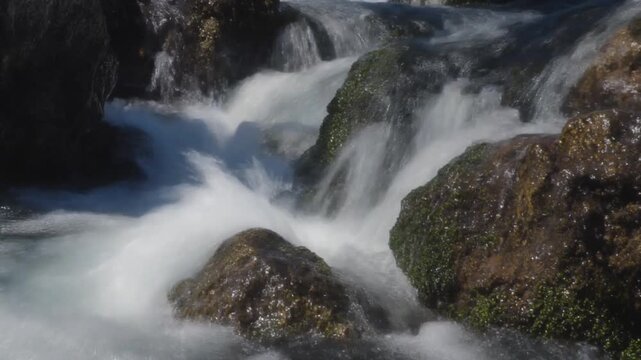 Serene waterfall cascading over moss-covered rocks in a clear, flowing river creating a tranquil natural scene