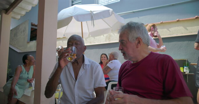 Two elderly friends sharing a meaningful conversation over drinks at a backyard barbecue, highlighting connection and joy during a lively outdoor gathering