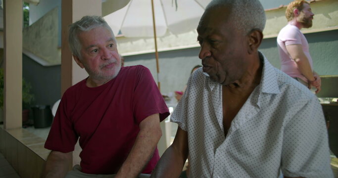 Two elderly friends sitting and conversing at a backyard barbecue, sharing meaningful dialogue and connection during a relaxed and casual outdoor gathering