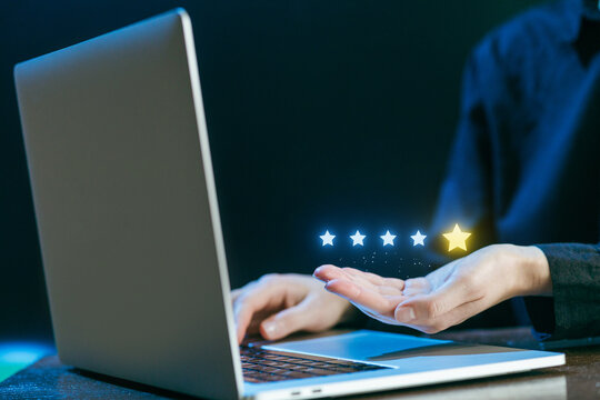 Hands reaching out for a five-star rating while using a laptop in a dark setting, highlighting digital reviews