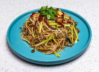 Enjoy this delicious Asian noodle dish, garnished with fresh vegetables and herbs, served on a bright blue plate. Perfect for healthy meals and culinary creations.