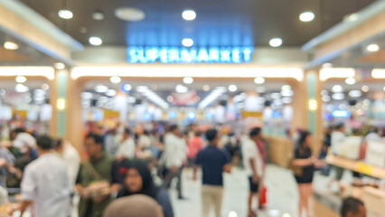 blurry image of a busy interior of a supermarket, the ambiance showing the self-service model in action with numerous people shopping in the aisles.