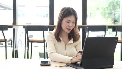 Young woman using a credit card to make online payments on her laptop in a modern cafe, representing digital lifestyle and e-commerce convenience. - Powered by Adobe