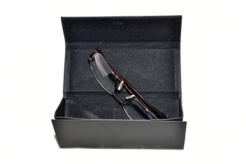 Dark colored glasses case and glasses with metal frames on white background.