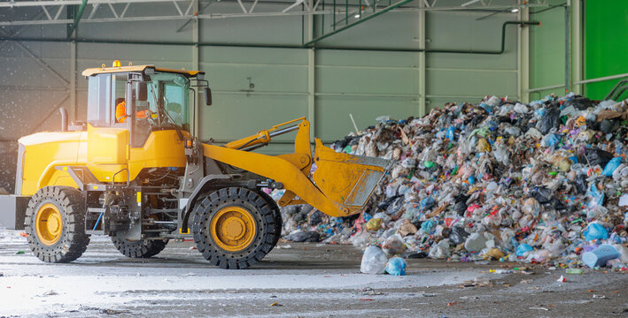 Yellow bulldozer in recycling plant sorting waste piles