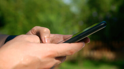 Closeup of man hands using a smartphone outdoors in a sunny garden.