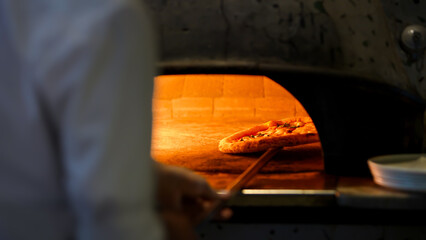 A pizza rests on a stone in a wood fired oven, with the fire heat cooking