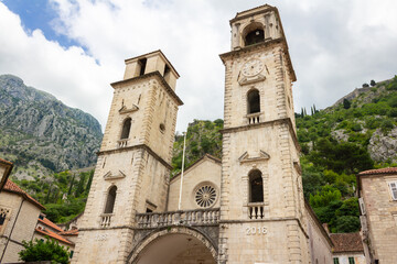 Fototapeta premium Kotor, Montenegro - June 6, 2025: The Cathedral of Saint Tryphon with its bell tower and clock tower. Mountains in the background of the Old Town Square.