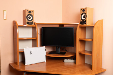 Workspace with monitor, speakers, power strip and white magnetic board on a wooden desk near a pink...