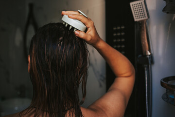 Naklejka premium Woman massages the scalp with a brush for hair growth. Woman combing damp hair in shower.