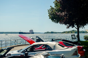 Summer car show on waterfront with a freight ship in the background