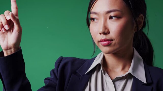 A woman in a dark blazer raises her finger, indicating a significant point in a discussion. The green backdrop emphasizes her gesture, highlighting focus and engagement in the topi