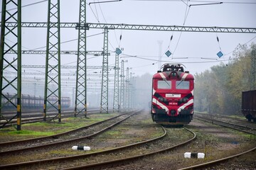 Red locomotive on railway tracks in industrial railyard
