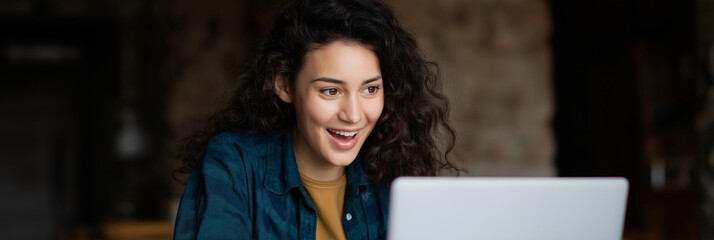 A joyful young woman is intently engaged with her laptop, expressing excitement and curiosity which symbolize endless possibilities in the digital age.
