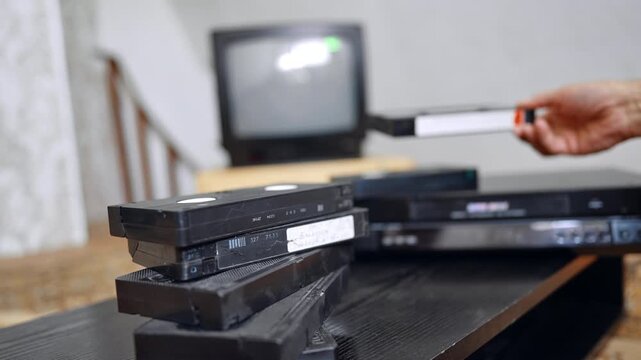 Pile of old VHS cassettes on the table. Male places some tapes on the recorder and puts one into the player.