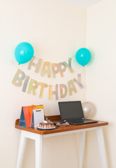 A cozy birthday setup on a wooden desk featuring a chocolate cake, colorful gift bags, cupcakes, a laptop, and festive decorations with balloons and a &ldquo;Happy Birthday&rdquo; banner. Perfect for celebrating 