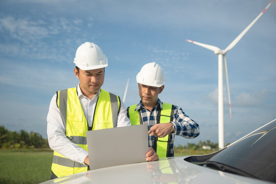 Renewable energy maintenance. Engineer using laptop computer checking system of wind turbine at windmill field farm station. Wind turbine energy storage system. Workers meeting to check around the are